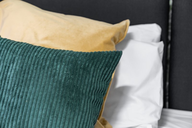 Bed with green ribbed cushion, yellow pillow and white bedding against dark headboard