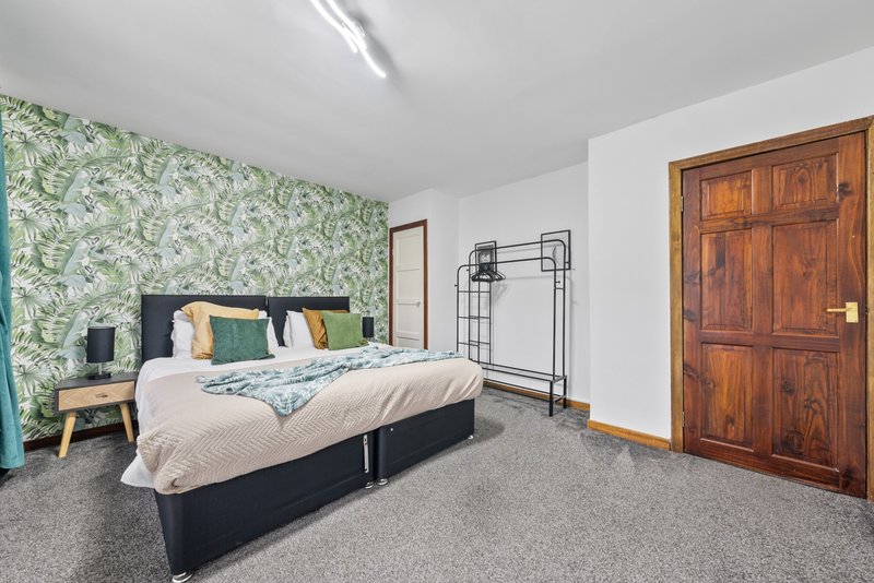 Spacious bedroom with double bed, green leaf wallpaper, wooden wardrobe and grey carpet