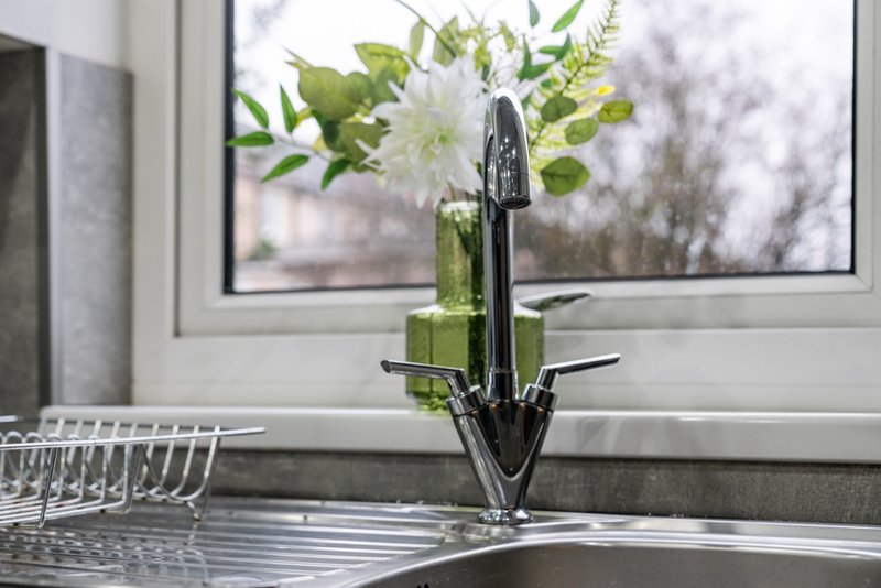 Kitchen sink with black faucet, fresh flowers in green vase, and window view