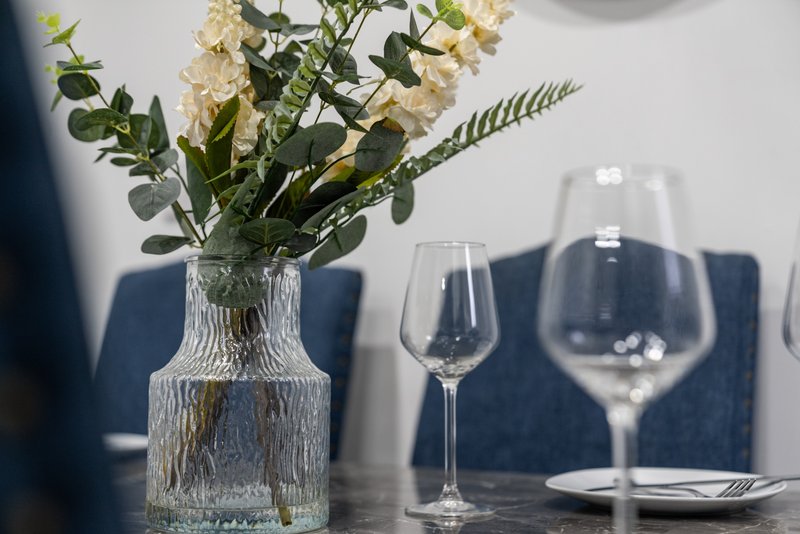 Dining table with textured vase, dried flowers, wine glasses and place setting