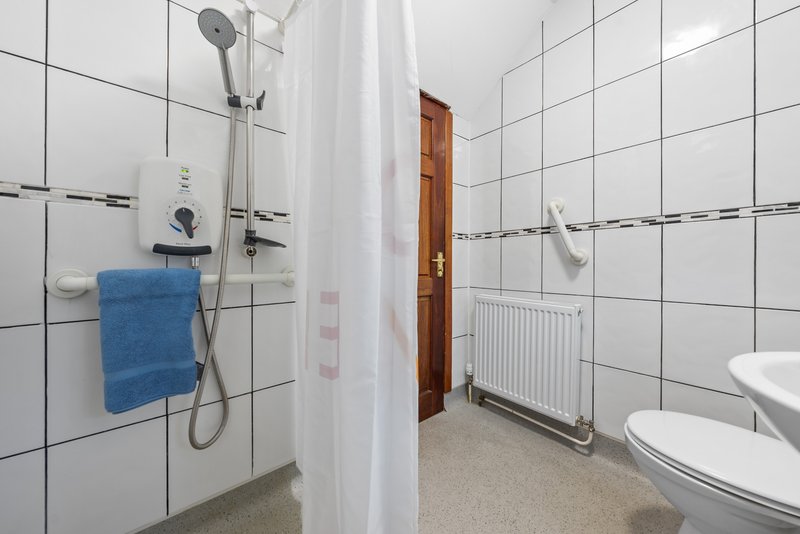 Bathroom with white tile walls, shower enclosure, blue towel, toilet and radiator
