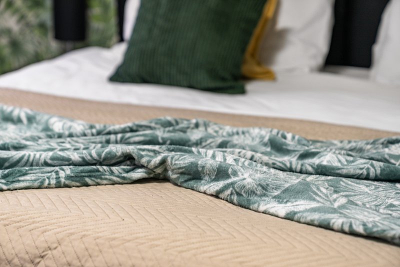 Bedroom detail showing unmade bed with green patterned duvet and decorative pillows