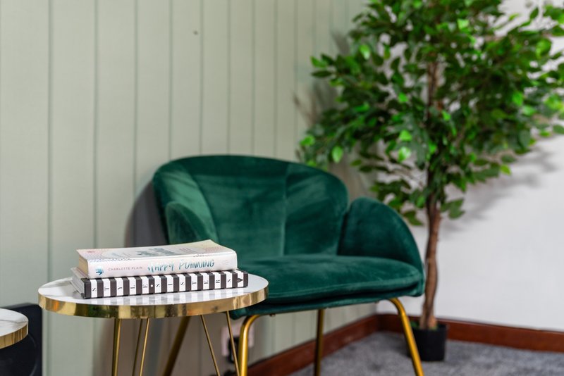 Green velvet armchair with side table, stacked books, potted plant and white wall
