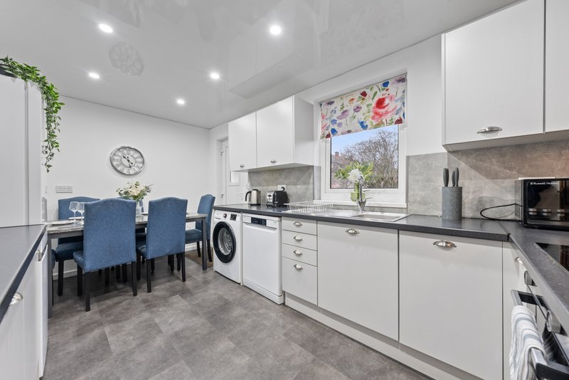 Modern kitchen with white cabinetry, integrated appliances, dining area with blue chairs