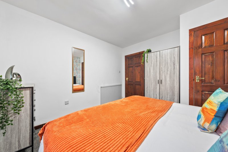 Bright bedroom with orange bedding, wooden wardrobe doors and potted plant