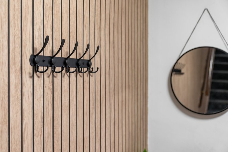 Entryway wall with vertical wood paneling, black coat hooks, and round mirror with leather strap