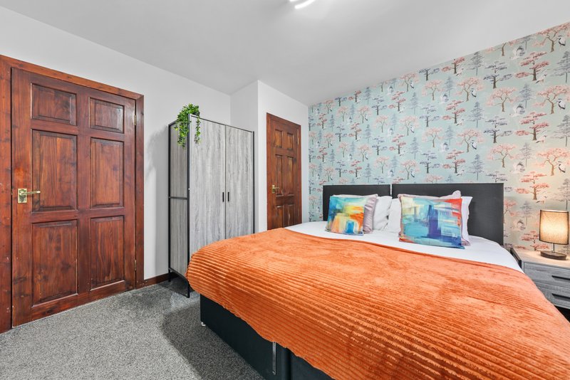 Bedroom with double bed, orange throw, patterned wallpaper, wooden doors and wardrobe