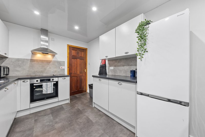 Modern white kitchen with gas hob, oven, large fridge-freezer and grey tile flooring