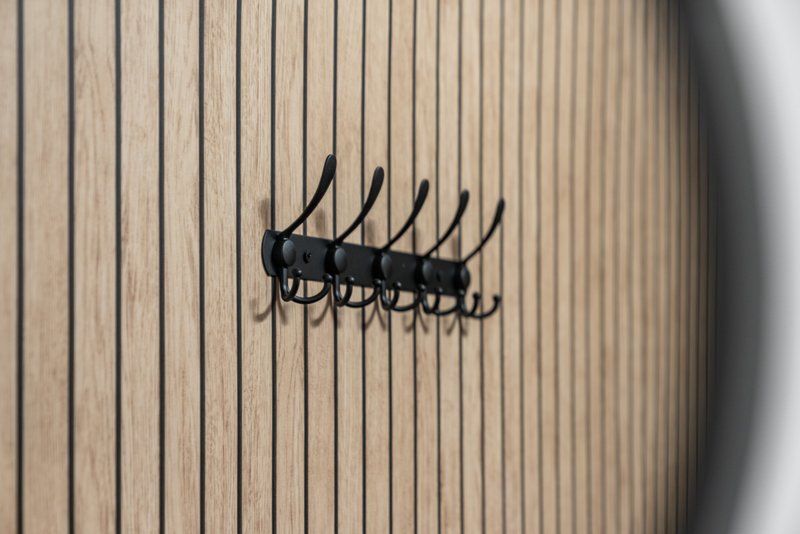 Black coat hook rack mounted on cream vertical panelled wall