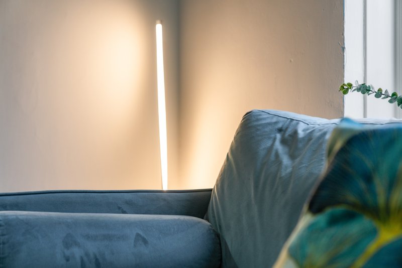Modern living room with blue upholstered sofa, wall-mounted linear light fixture, and potted plant