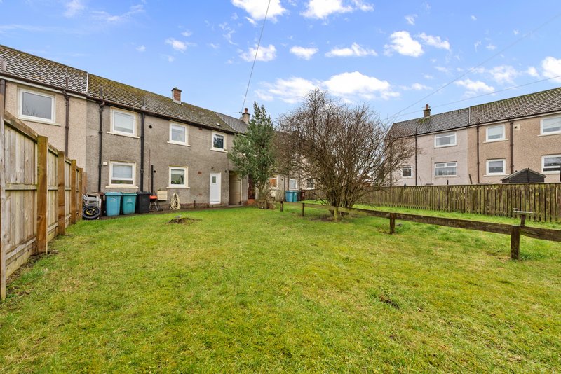 Communal green garden area with wooden benches, flanked by stone terraced houses