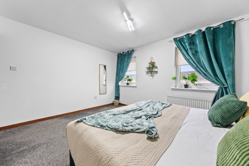 Bright bedroom with double bed, teal curtains, windows with plants and radiator