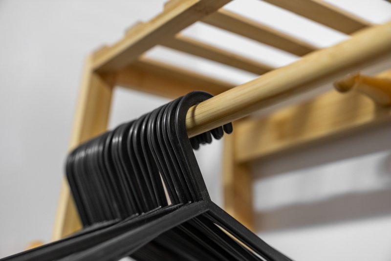 Wooden clothing rack with black plastic hangers against white wall