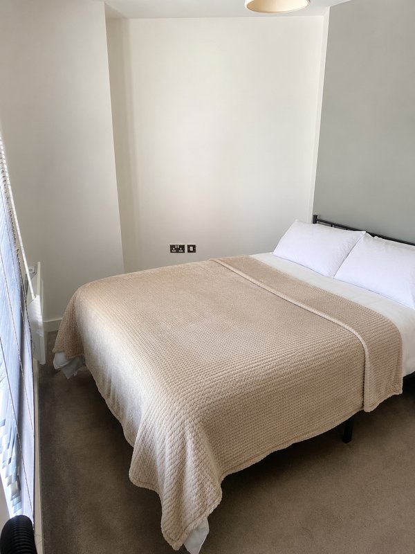 Minimal bedroom with double bed, beige bedding, white pillows and plain walls