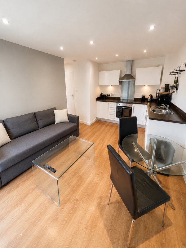 Open-plan living and kitchen area with grey sofa, dining table, and modern white kitchen units