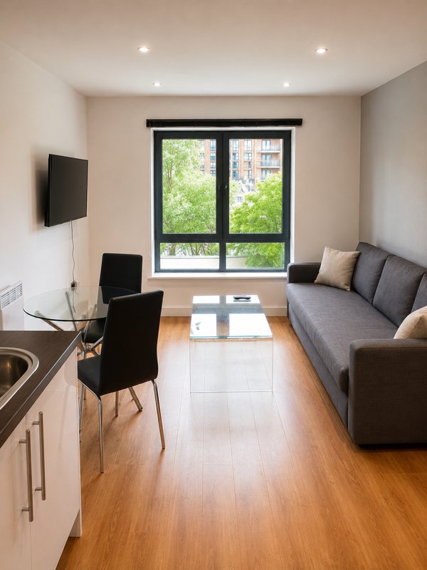 Modern studio apartment with sofa, desk, wall-mounted TV and large windows overlooking trees
