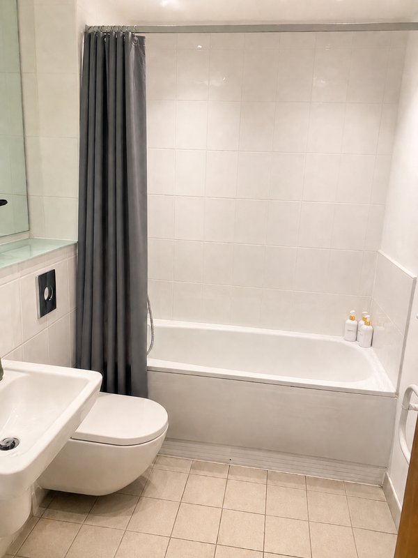 Clean bathroom with white toilet, sink, bathtub, grey shower curtain and tiled floor