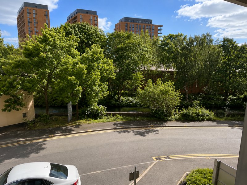 View of residential street with parked car, trees, and apartment buildings in background