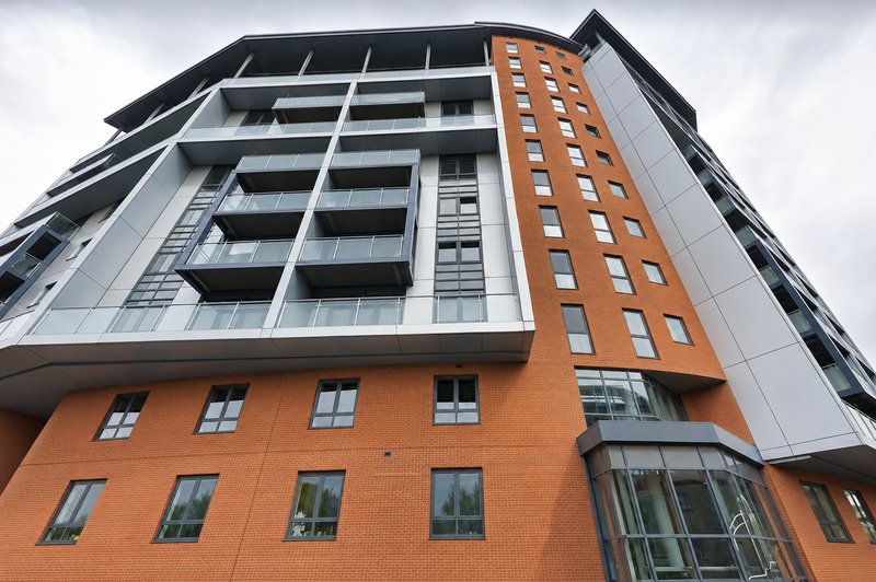 Modern residential building exterior with orange brick base and grey upper levels, multiple windows and balconies