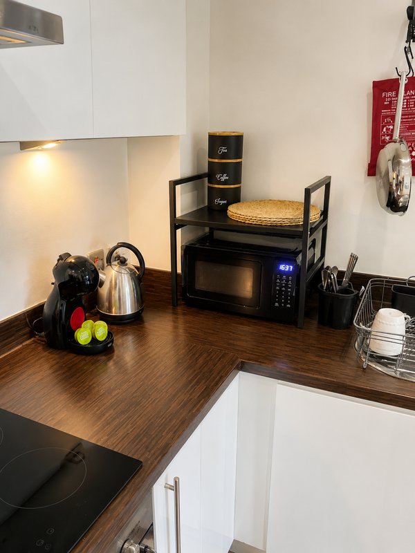 Compact kitchen corner with microwave, kettle, storage shelf and wooden countertop