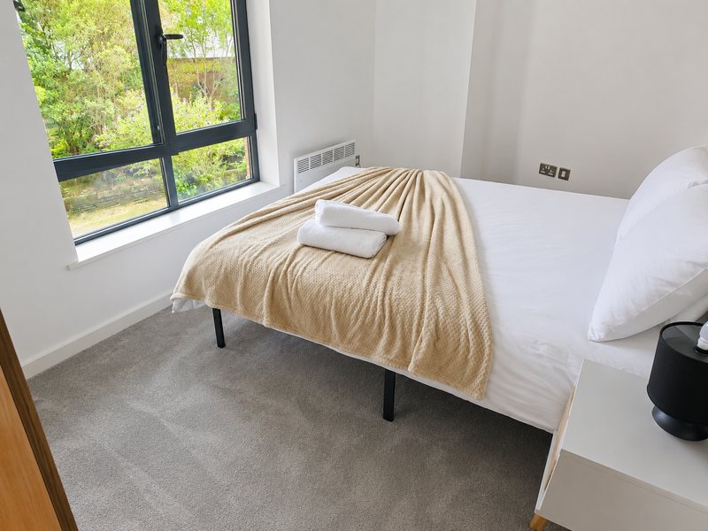 Bright bedroom with single bed, cream throw blanket, white pillows, and large window overlooking garden