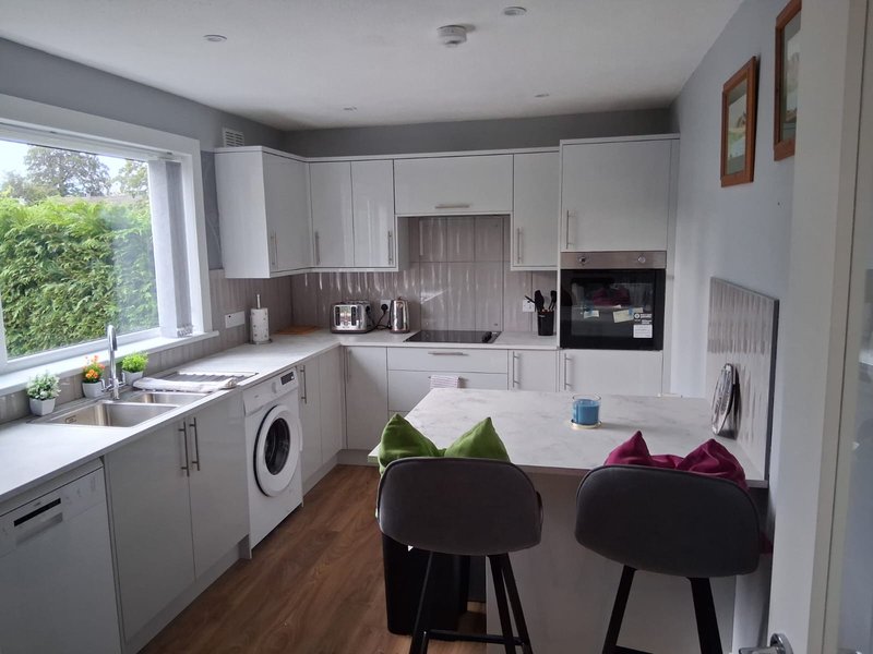 Modern kitchen with white cabinetry, dining island, bar stools, and garden view through window