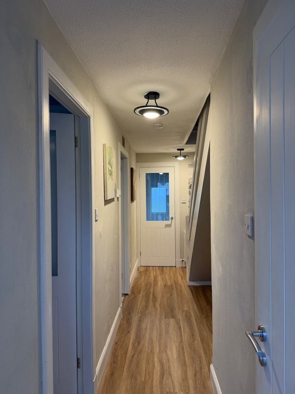 Long hallway with white walls, wooden floor, ceiling lights and multiple doors