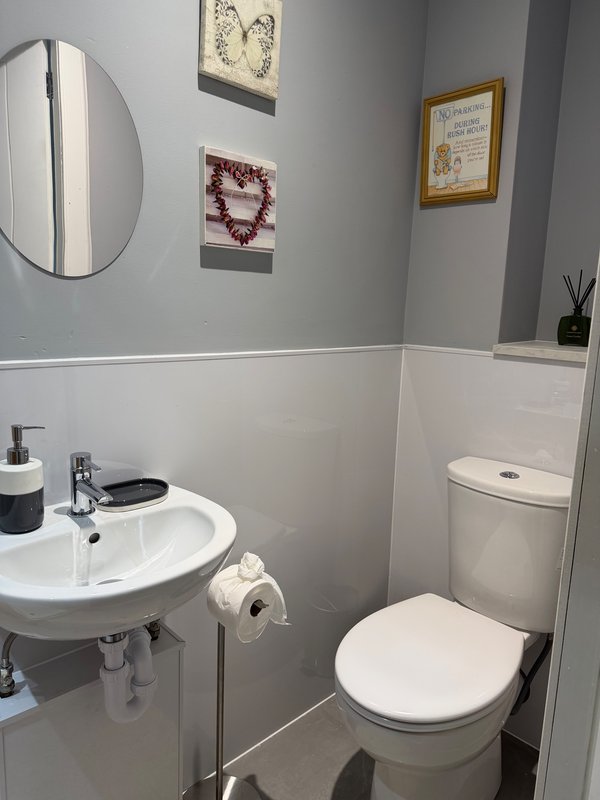 Bathroom with white sink, toilet, circular mirror, and framed wall art
