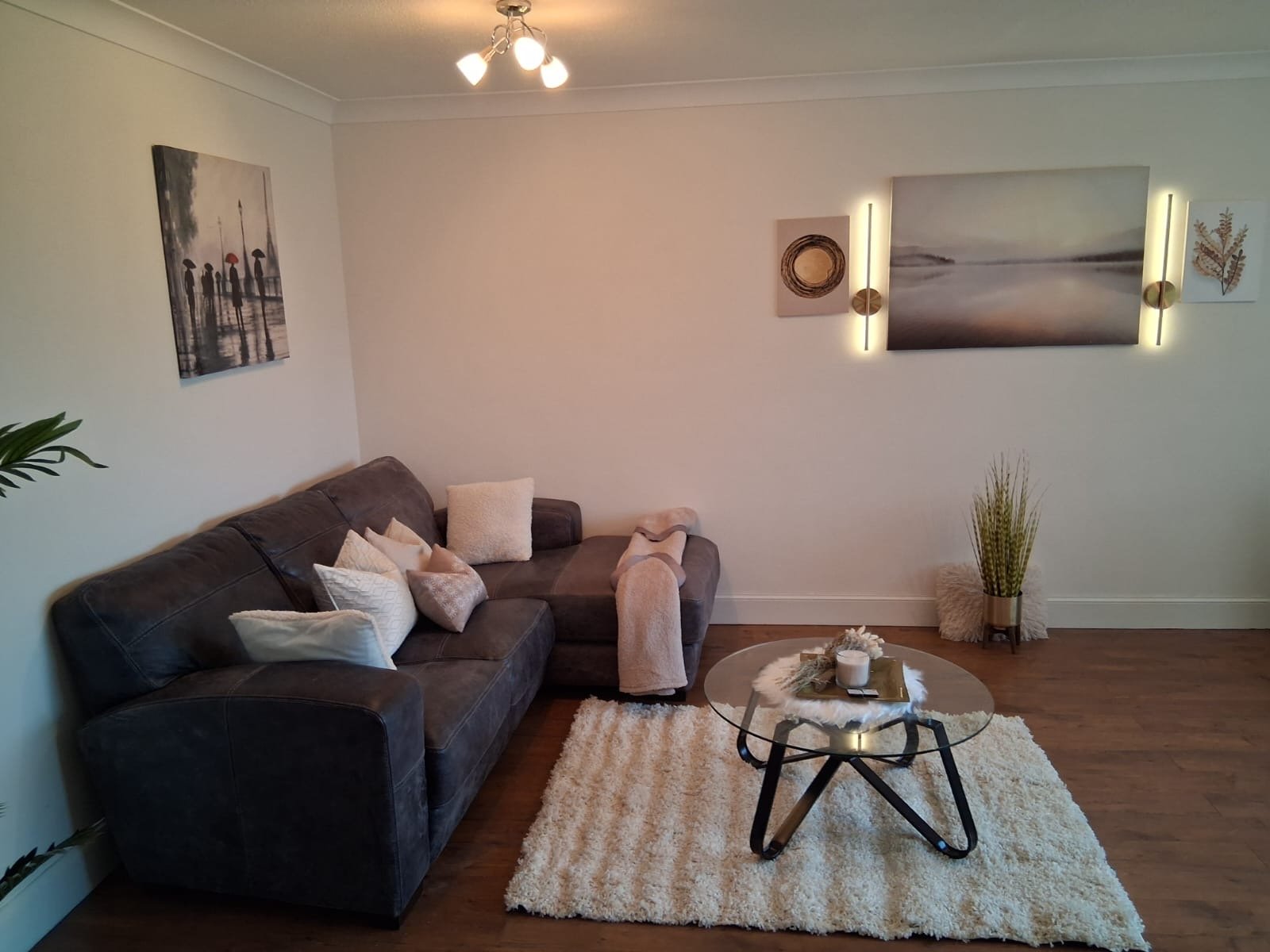 Living room with dark sofa, glass coffee table, wall art, and pendant lighting