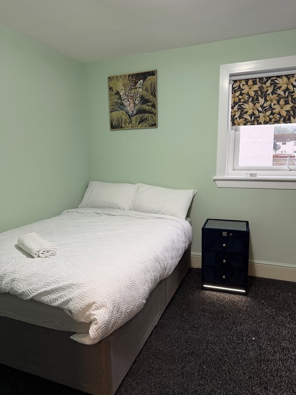 Bedroom with double bed, white bedding, mint green walls, black nightstand and window