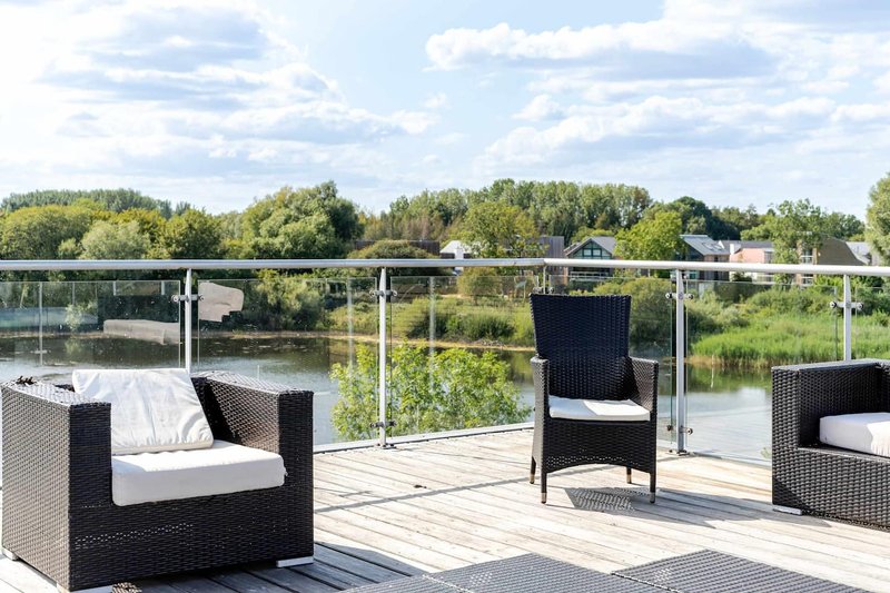 Waterfront deck with black rattan seating, white cushions, and river view beyond metal railings