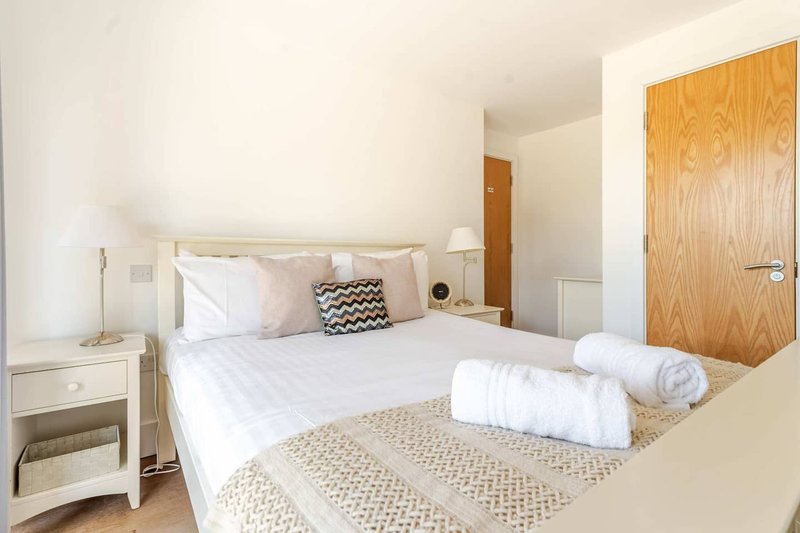 Bright bedroom with double bed, white bedding, wooden door, and bedside lamp
