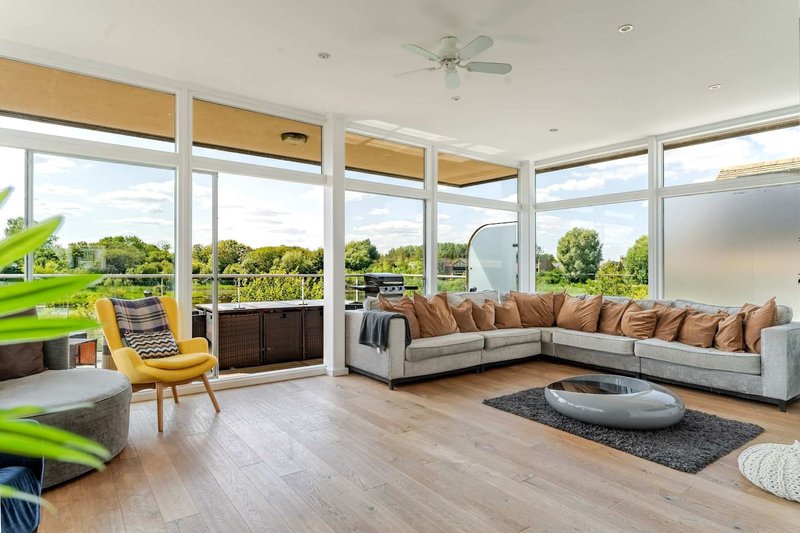 Modern living room with large windows, beige corner sofa, yellow armchair, wooden floors and garden views