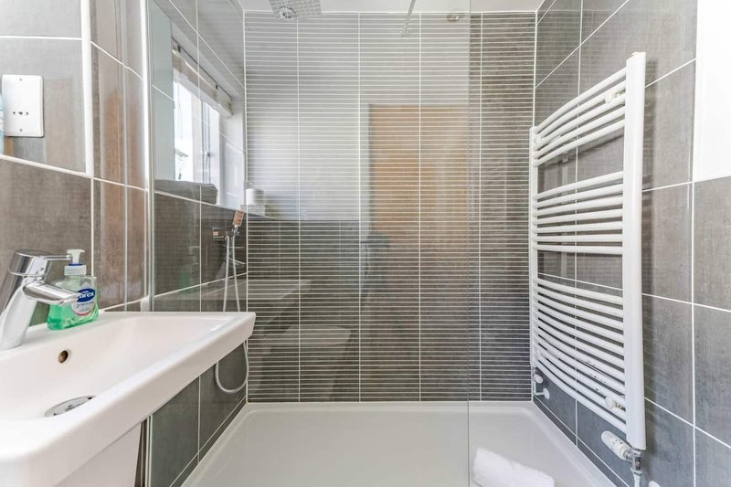 Modern bathroom with white sink, glass shower enclosure, heated towel rail and tile walls