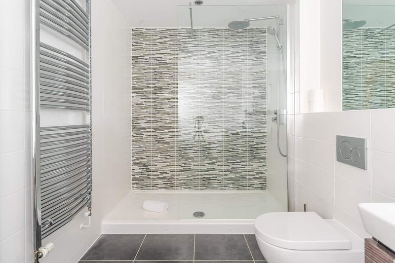 Modern bathroom with walk-in shower, striped tile feature wall, towel radiator and toilet