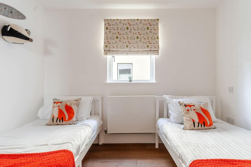 Bright twin bedroom with two single beds, white bedding, red blankets and patterned cushions
