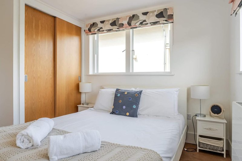 Bright bedroom with double bed, wooden wardrobe, bedside table and window with patterned valance