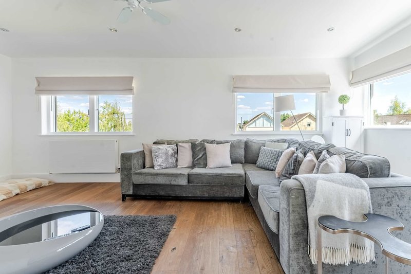 Bright open-plan living room with grey corner sofa, wooden floor, and garden views