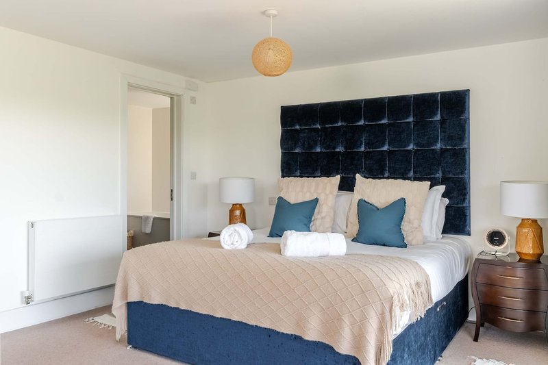Modern bedroom with blue quilted headboard, neutral bedding, wooden nightstands and pendant light