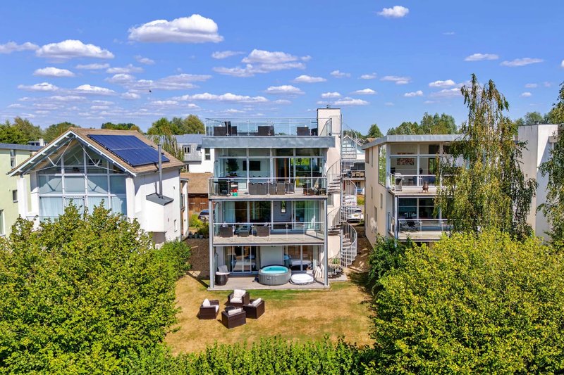 Modern multi-story residential building with balconies, garden, and neighboring properties visible
