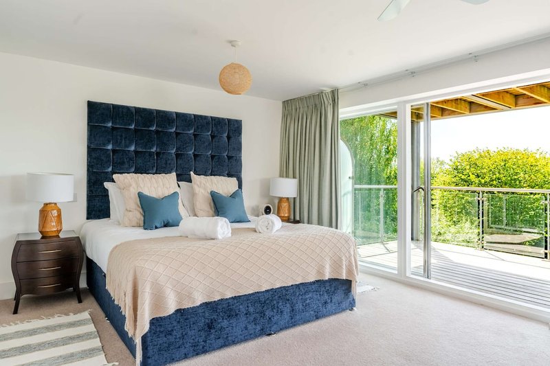 Bright modern bedroom with navy upholstered bed, white bedding, glass doors opening to balcony