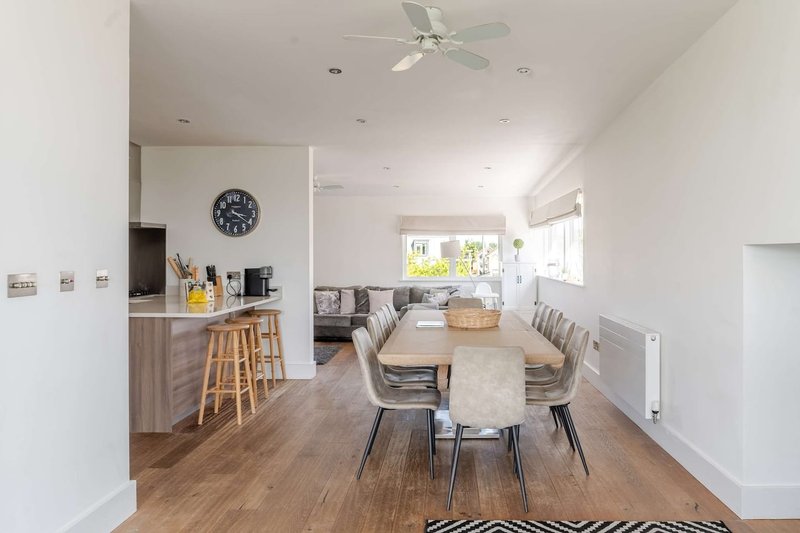 Open-plan kitchen and dining area with wooden flooring, dining table, bar seating, and ceiling fan