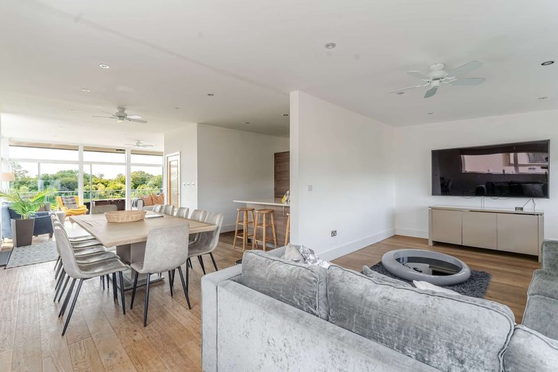Open-plan living area with dining table, grey sofa, wall-mounted TV, and wooden flooring