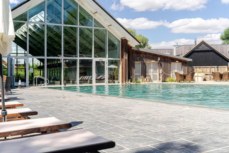 Modern outdoor swimming pool with loungers, glass pavilion and surrounding buildings