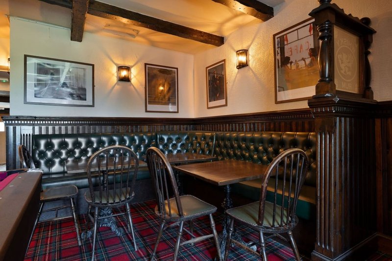 Dining area with black leather chesterfield seating, wooden table, chairs and framed wall art