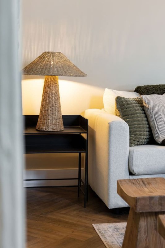 Living room corner with grey sofa, woven table lamp, black side table and wooden stool