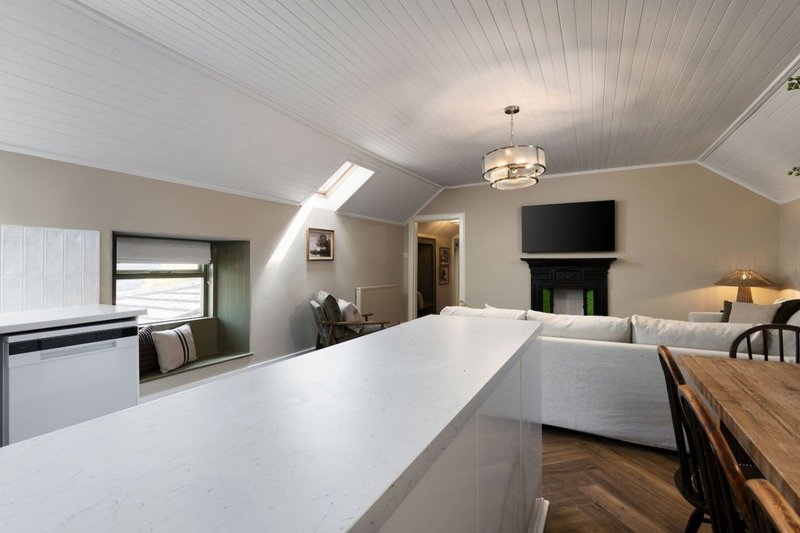 Open-plan attic space with white kitchen island, sofa, fireplace and mounted TV