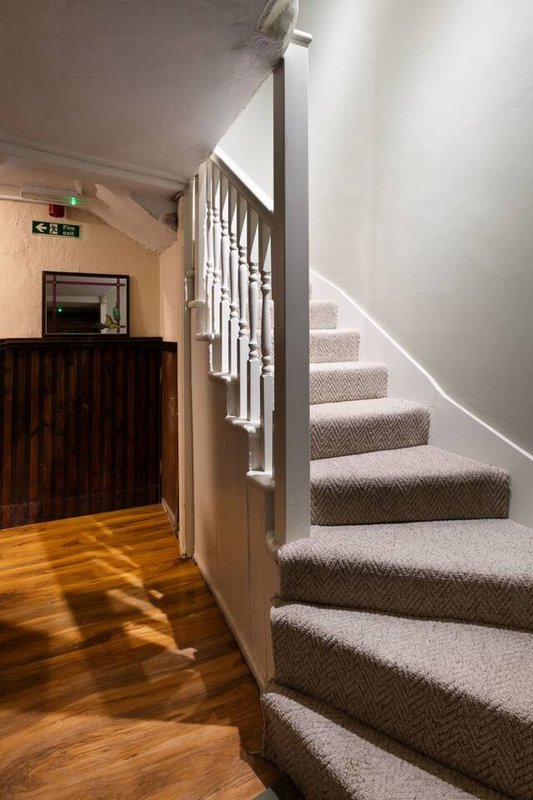 Hallway with wooden floor, staircase with carpet runner, white railings and modern lighting