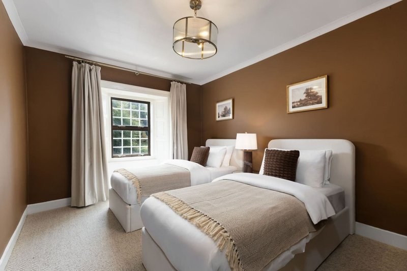 Bedroom with two twin beds, brown walls, window with curtains and ceiling light fixture