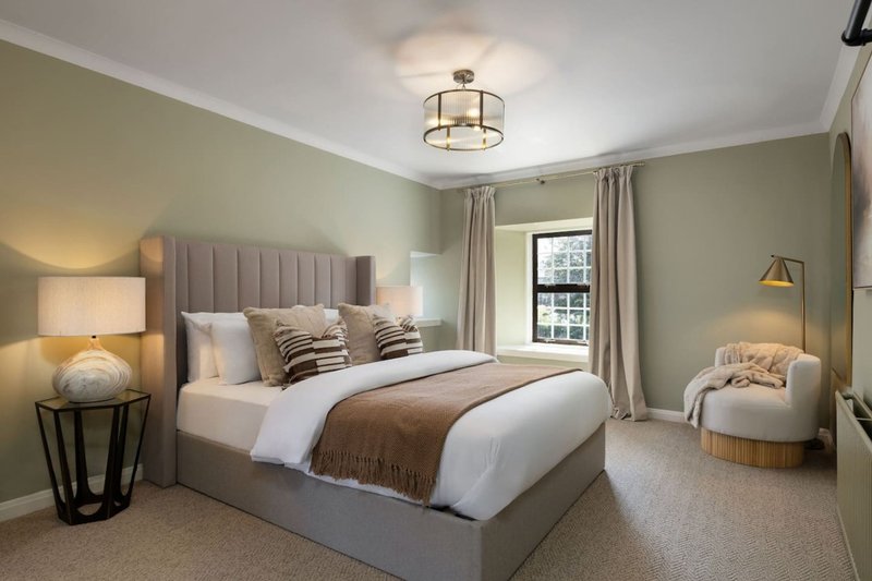 Spacious bedroom with upholstered bed, bedside lamps, armchair, and large window